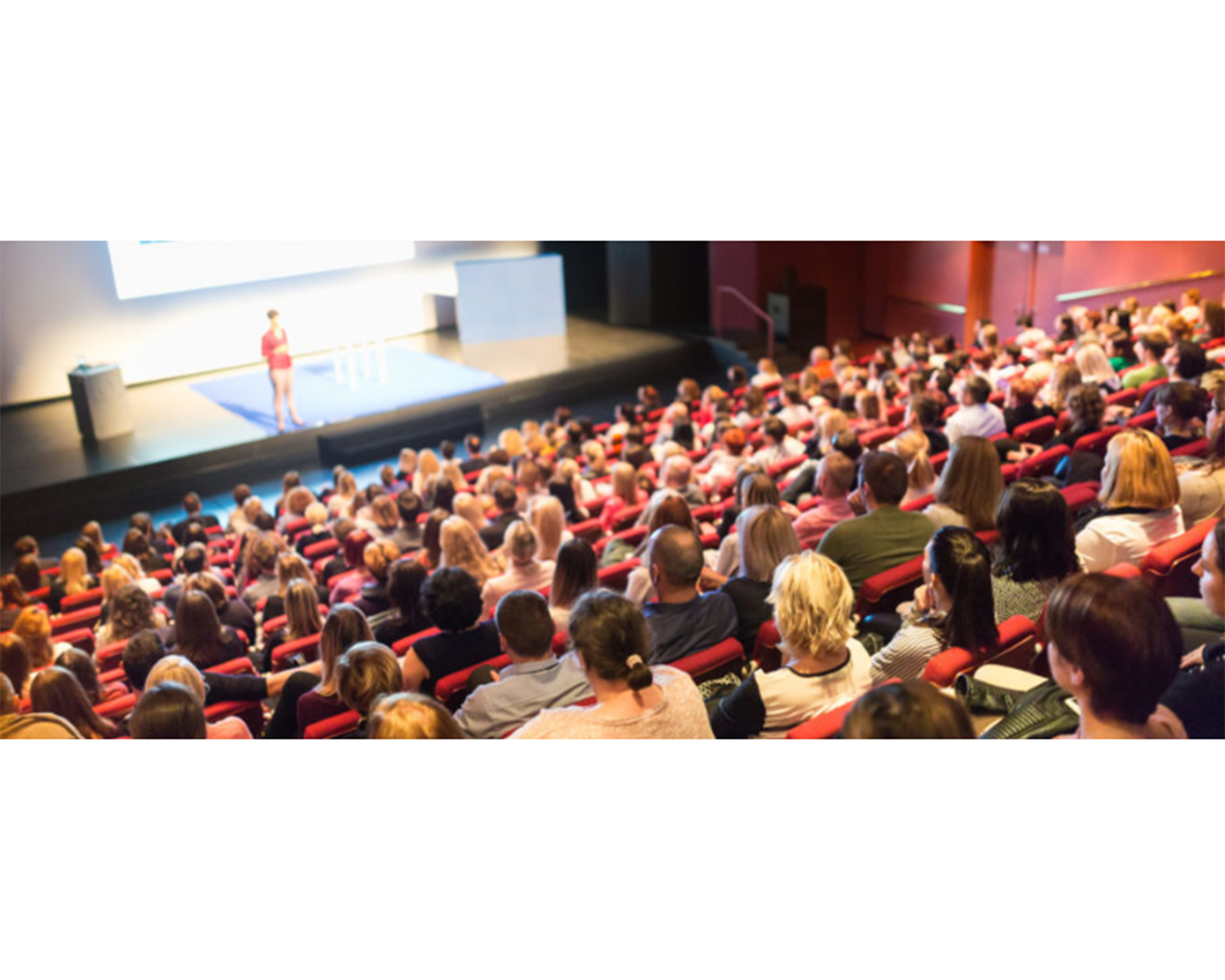 A photo from the back of a lecture hall shows a large audience watching a speaker on the stage.