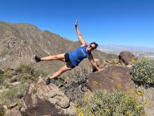 Dr. Terri Laguna does a side plank on a hike, wearing a blue shirt and black shorts. 